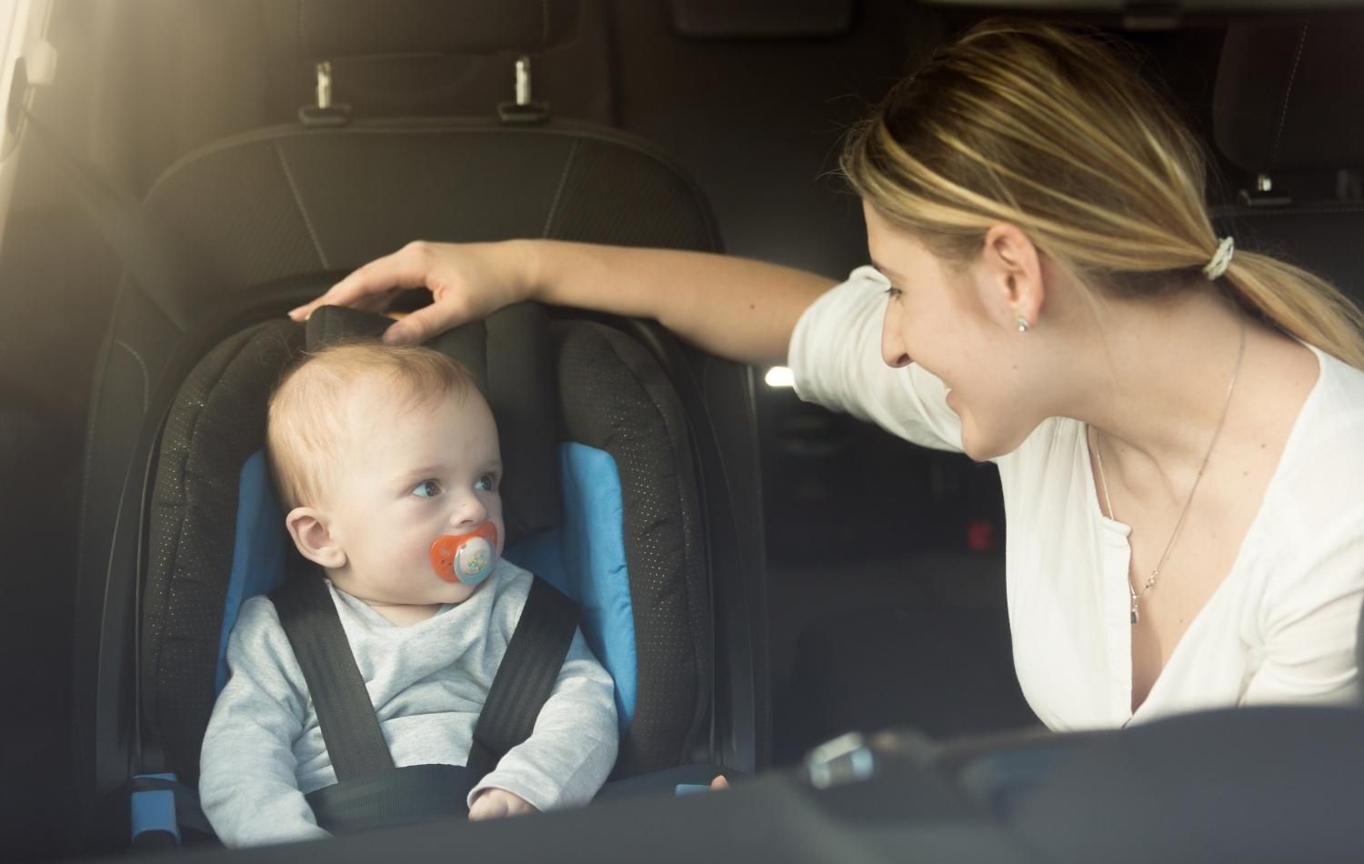 A mother with a baby in a car seat in the back of a black car transport